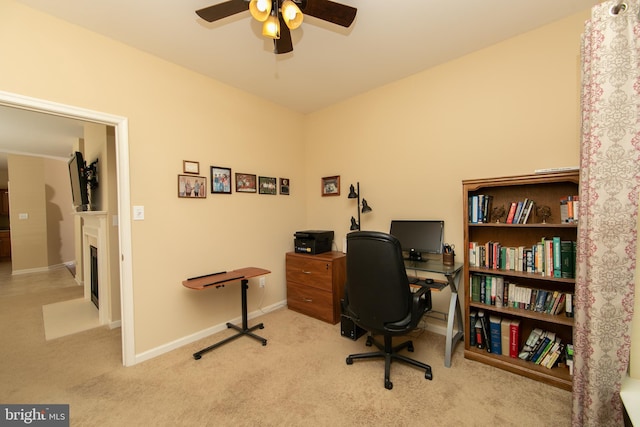 home office featuring carpet, a fireplace, a ceiling fan, and baseboards