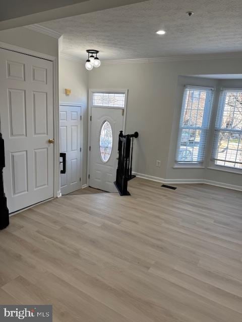 foyer entrance with ornamental molding, plenty of natural light, and light wood-style flooring