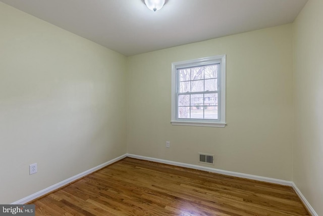 unfurnished room featuring wood finished floors, visible vents, and baseboards