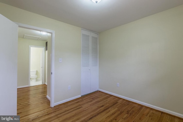 unfurnished bedroom featuring attic access, baseboards, a closet, and wood finished floors