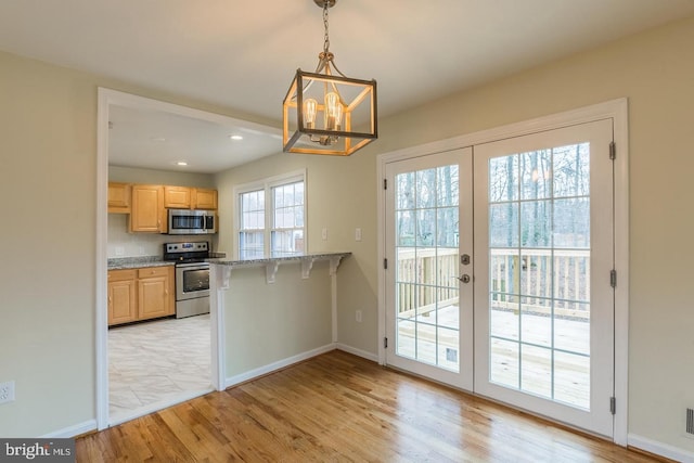 kitchen with light brown cabinets, a breakfast bar, light wood-style floors, french doors, and appliances with stainless steel finishes