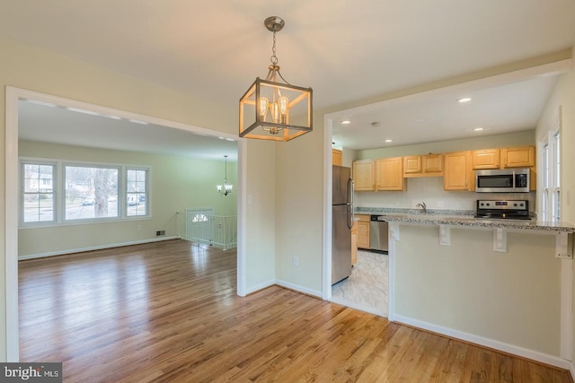 kitchen with light wood-style flooring, appliances with stainless steel finishes, open floor plan, light brown cabinets, and a notable chandelier