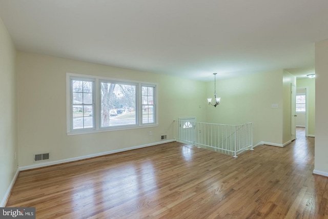 spare room with a wealth of natural light, visible vents, a notable chandelier, and wood finished floors