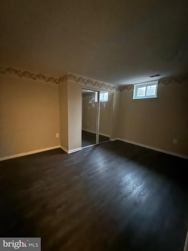 basement featuring dark wood-type flooring, visible vents, and baseboards