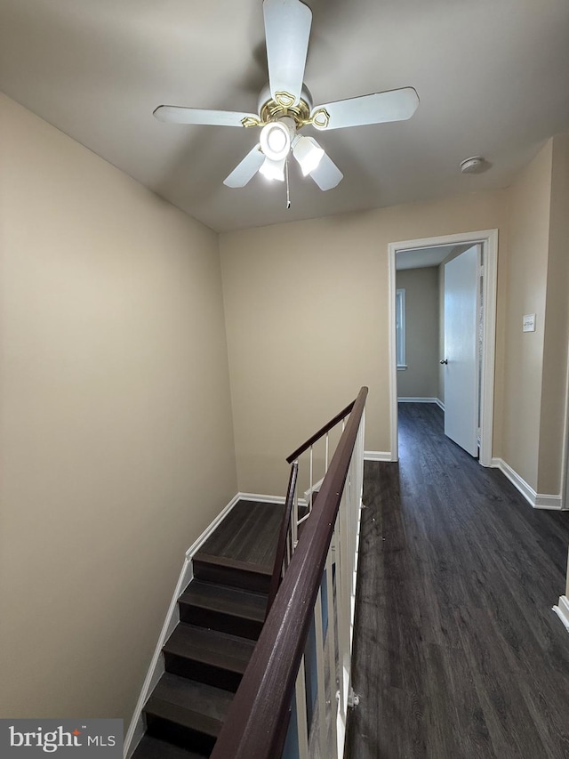 hall featuring dark wood-style floors, baseboards, and an upstairs landing