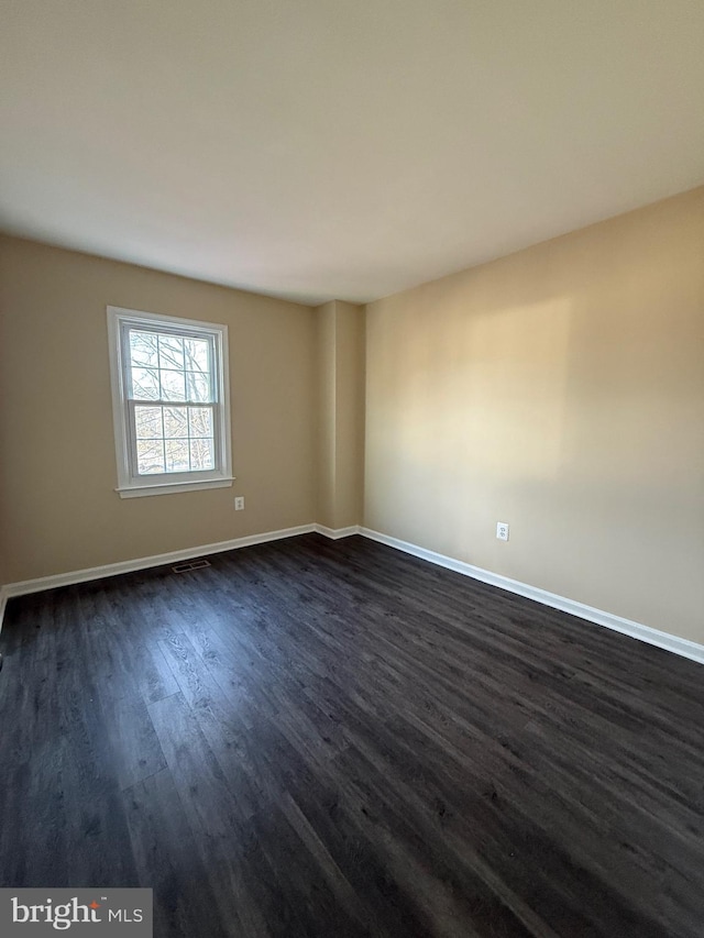 empty room with visible vents, dark wood finished floors, and baseboards