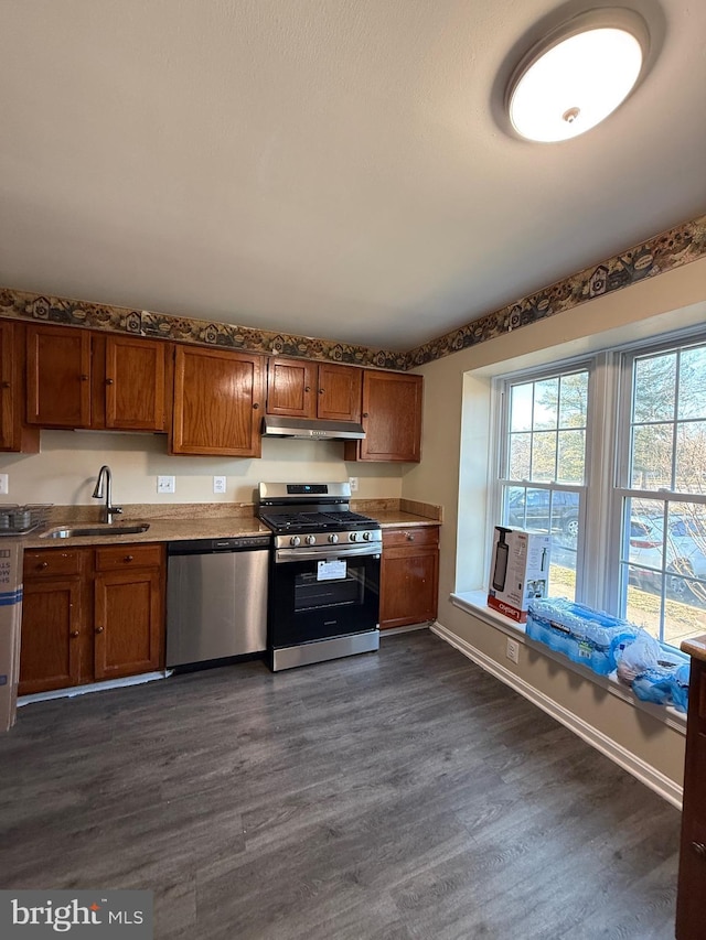 kitchen featuring under cabinet range hood, appliances with stainless steel finishes, dark wood-type flooring, and a sink