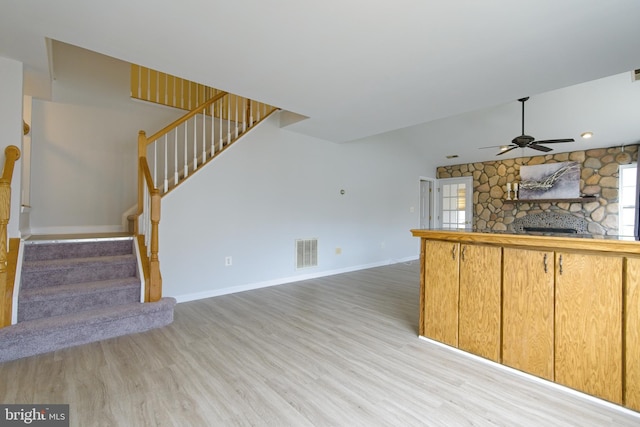 unfurnished living room featuring baseboards, visible vents, stairs, a stone fireplace, and light wood-type flooring