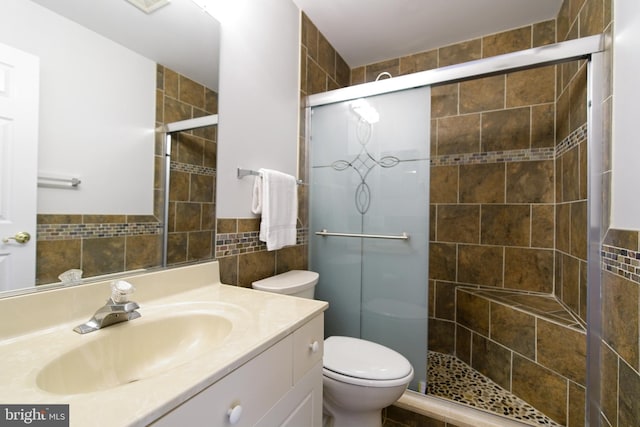 full bathroom with toilet, a stall shower, tile walls, and vanity