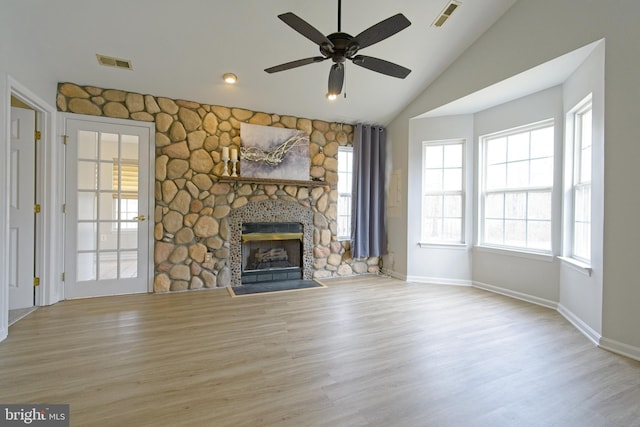 unfurnished living room featuring lofted ceiling, visible vents, a stone fireplace, and wood finished floors