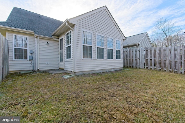 rear view of property featuring roof with shingles, fence, and a lawn