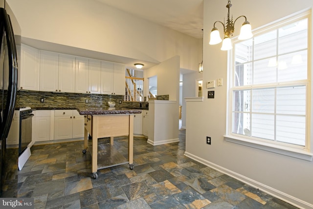 kitchen featuring stove, white cabinetry, baseboards, decorative backsplash, and stone finish floor