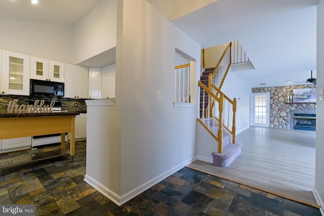 kitchen featuring black microwave, stone finish floor, dark countertops, and white cabinetry