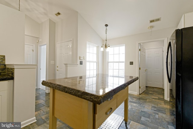 kitchen featuring visible vents, stone finish floor, dark stone countertops, decorative light fixtures, and freestanding refrigerator