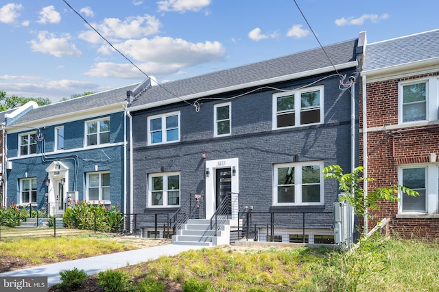 townhome / multi-family property featuring roof with shingles and brick siding