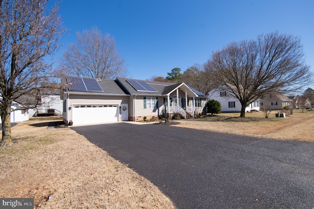 ranch-style house featuring driveway, roof mounted solar panels, a porch, an attached garage, and crawl space