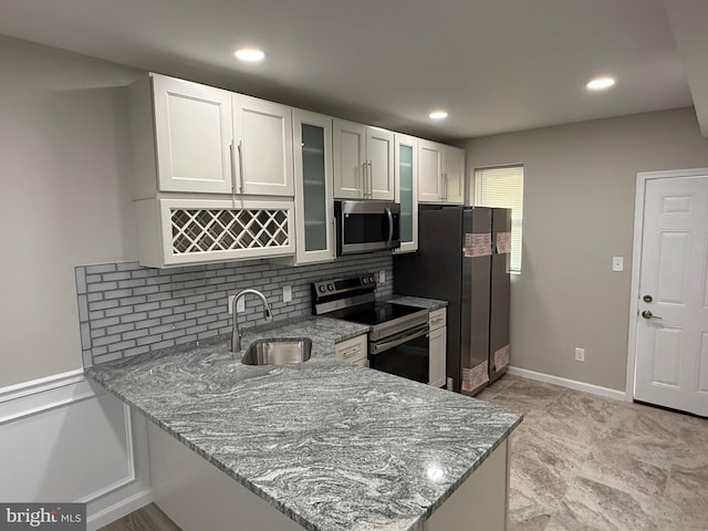 kitchen featuring light stone counters, appliances with stainless steel finishes, glass insert cabinets, a sink, and a peninsula