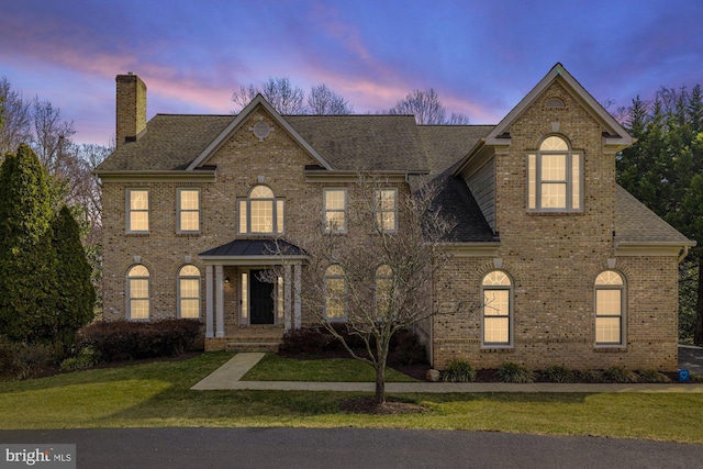 colonial inspired home featuring a lawn, brick siding, and a chimney