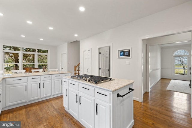 kitchen featuring a kitchen island, stainless steel gas cooktop, recessed lighting, wood finished floors, and white cabinets