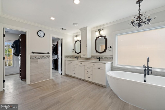 full bath featuring ornamental molding, double vanity, wainscoting, a freestanding tub, and tile walls