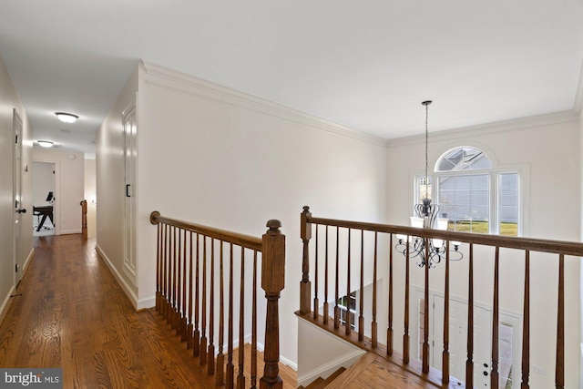 hallway with wood finished floors, baseboards, an inviting chandelier, crown molding, and an upstairs landing