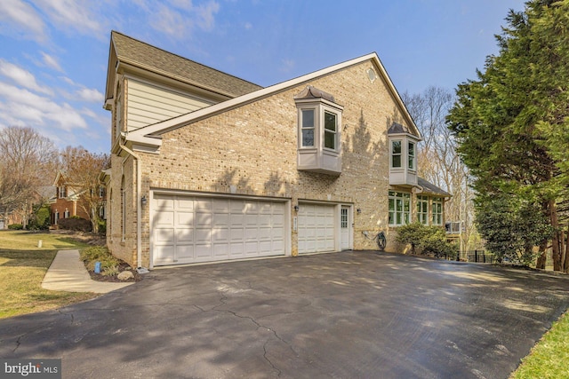 view of side of property featuring brick siding, an attached garage, and driveway