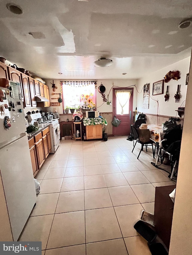 kitchen featuring white appliances, wainscoting, under cabinet range hood, and light tile patterned flooring