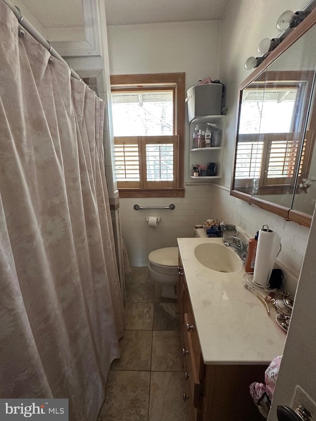 bathroom with toilet, tile walls, vanity, and a healthy amount of sunlight