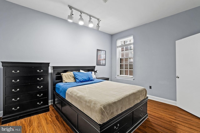 bedroom featuring track lighting, wood finished floors, and baseboards