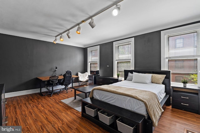 bedroom featuring wood finished floors, rail lighting, and baseboards