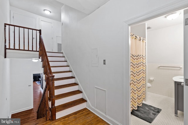 staircase with wainscoting, wood finished floors, and tile walls