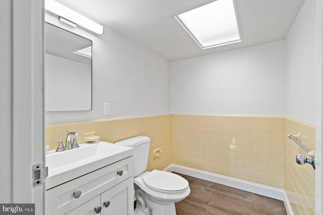 half bath featuring toilet, wood finished floors, vanity, tile walls, and wainscoting