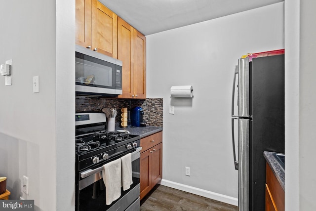 kitchen with baseboards, appliances with stainless steel finishes, decorative backsplash, dark wood-style floors, and dark countertops