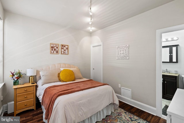 bedroom with ensuite bathroom, a sink, baseboards, dark wood finished floors, and rail lighting