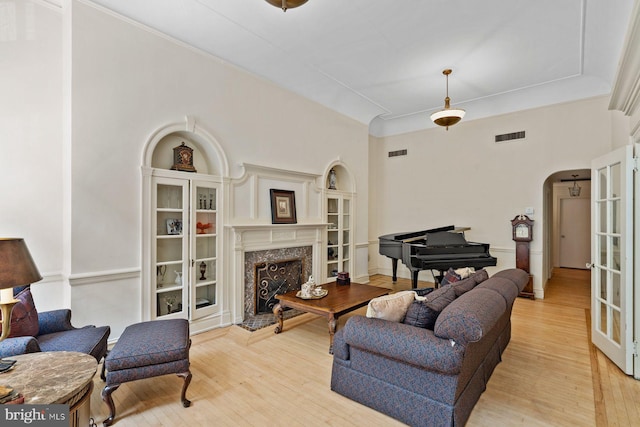 living area featuring arched walkways, a premium fireplace, light wood-type flooring, and visible vents