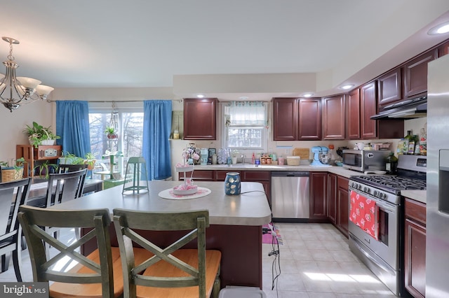 kitchen with under cabinet range hood, stainless steel appliances, reddish brown cabinets, and light countertops