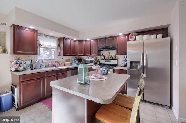 kitchen with a center island, under cabinet range hood, light countertops, appliances with stainless steel finishes, and a sink