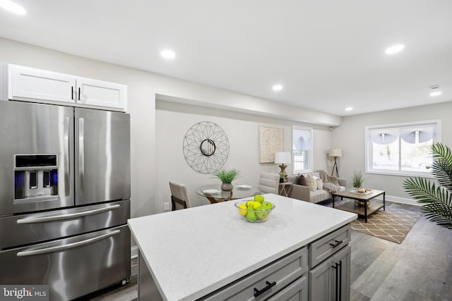 kitchen featuring stainless steel fridge with ice dispenser, a kitchen island, wood finished floors, light stone countertops, and recessed lighting