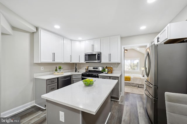 kitchen with appliances with stainless steel finishes, dark wood-style flooring, white cabinetry, and a kitchen island