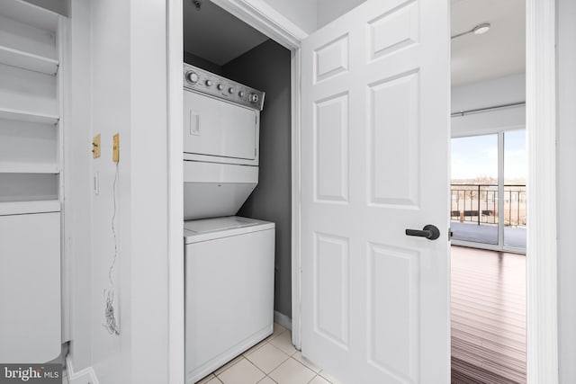 laundry area featuring stacked washer / dryer, laundry area, baseboards, and light tile patterned floors