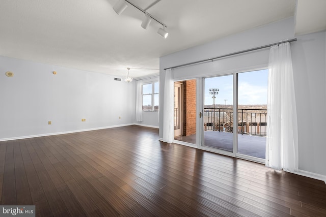 spare room with dark wood-style floors, rail lighting, visible vents, and baseboards