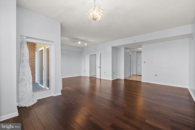 empty room with a notable chandelier, baseboards, and wood finished floors