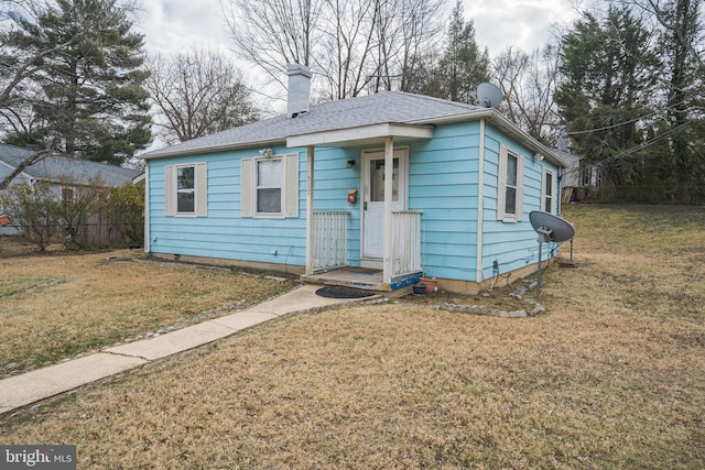 bungalow with roof with shingles, a chimney, and a front yard