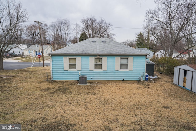 back of property featuring a yard, a shed, roof with shingles, and an outdoor structure