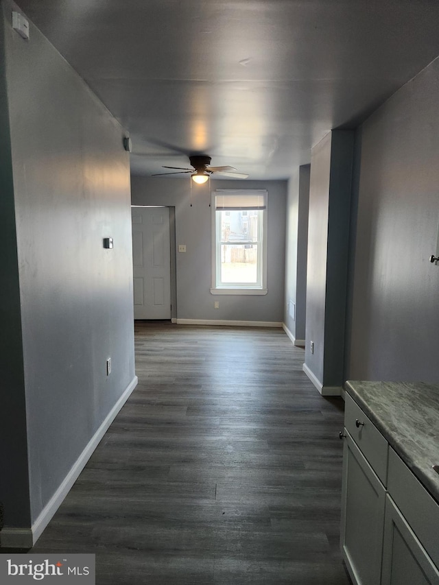 interior space with a ceiling fan, dark wood-style flooring, and baseboards