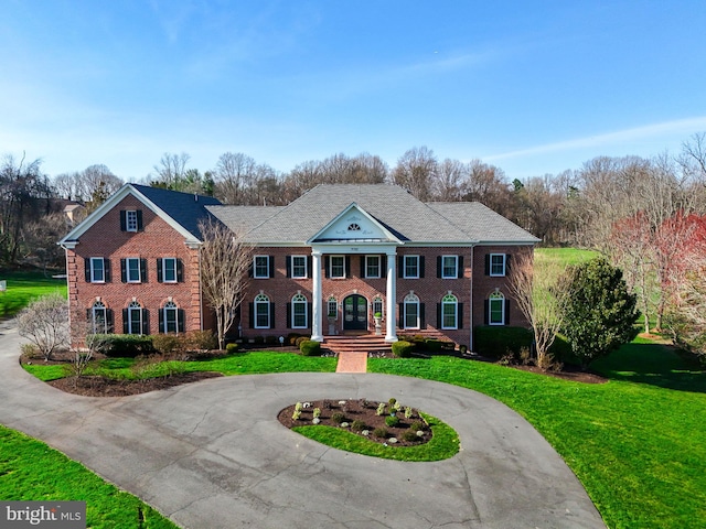 greek revival house featuring a front yard, brick siding, and curved driveway