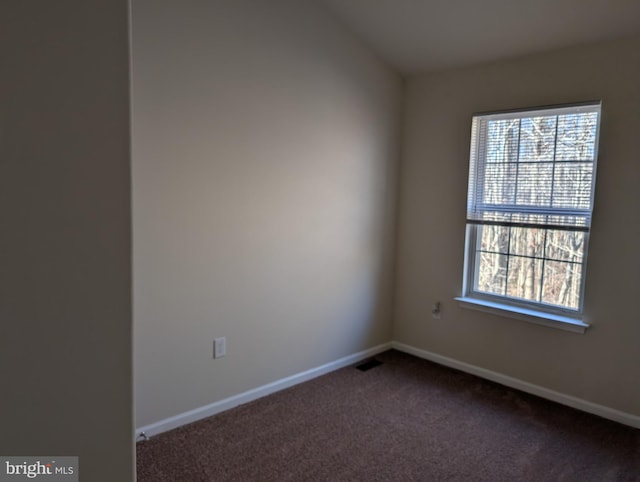 empty room featuring plenty of natural light, visible vents, dark carpet, and baseboards