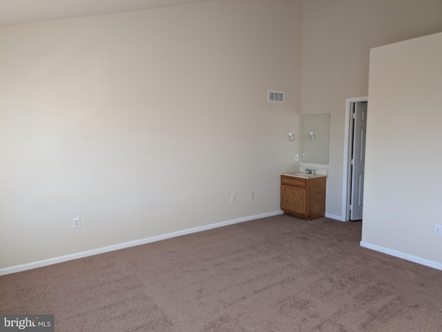 unfurnished bedroom featuring visible vents, baseboards, a towering ceiling, carpet floors, and a sink