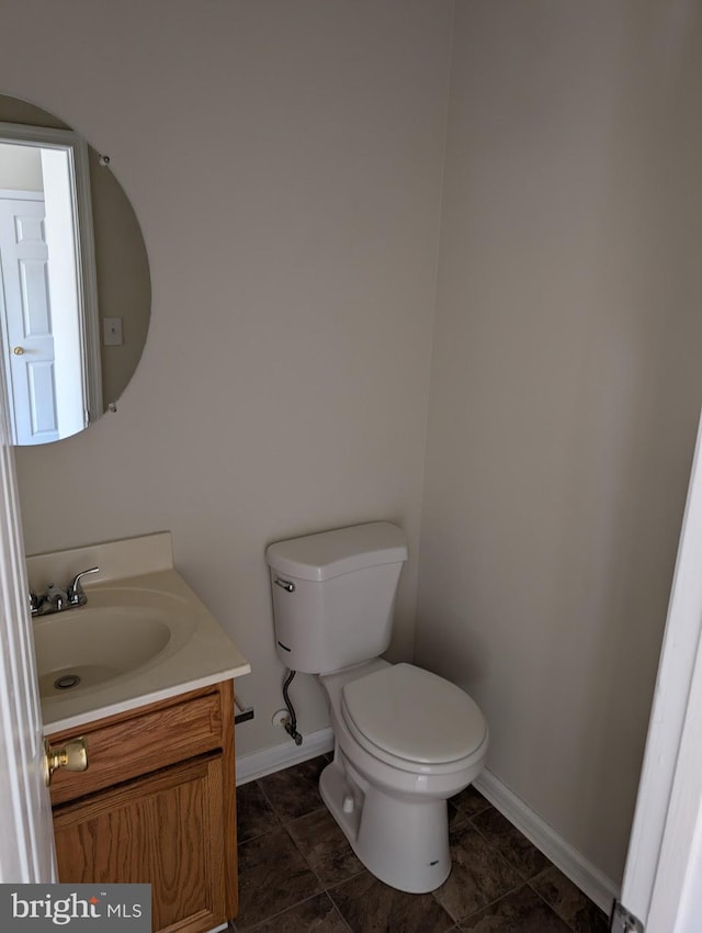 half bath with toilet, baseboards, and vanity