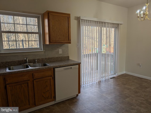 kitchen featuring decorative backsplash, dark countertops, an inviting chandelier, white dishwasher, and a sink